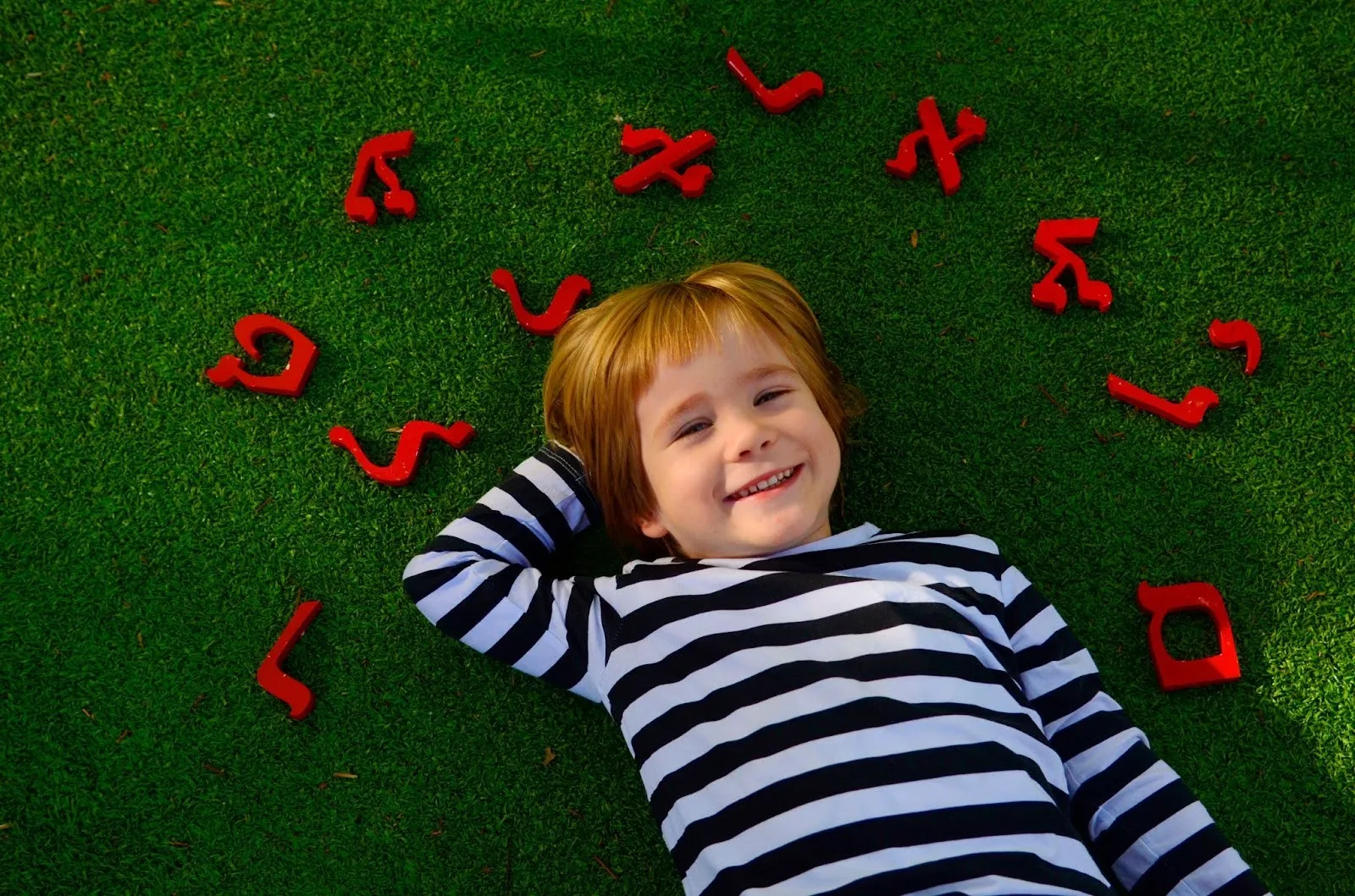 Image of a young boy laying in the grass surrounded by red Hebrew letters.